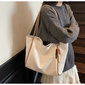 Detail of cream tote bag with V-shaped woven texture and wooden bead charm detail