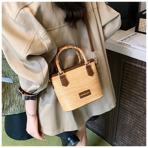 Detail of straw woven bucket bag with bamboo handle and brown leather straps