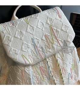 Detail of white embossed fabric on backpack with colorful stitching and geometric textures