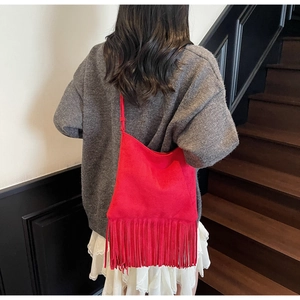Detalle de bolso rojo de ante con flecos sobre una falda de encaje blanca de modelo