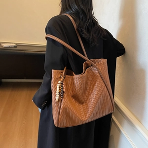 Detail of a brown woven tote bag featuring a textured weave and elegant wooden bead charm