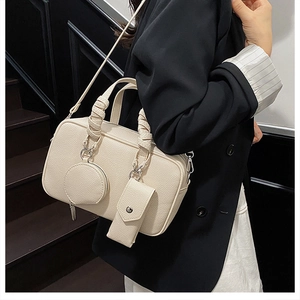 Detail of cream Boston bag with pleated handles and detachable pouch charms on suit