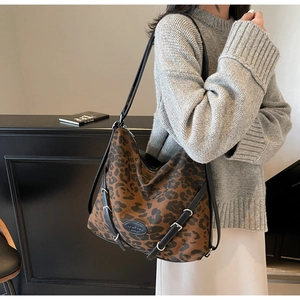 Detail of leopard print tote bag with black leather straps and metal buckles