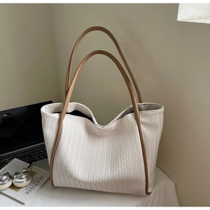 Close-up of off-white woven tote bag with brown leather straps and fine V-shaped texture