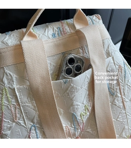 Detail of white quilted backpack featuring a rear pocket with smartphone for storage capacity