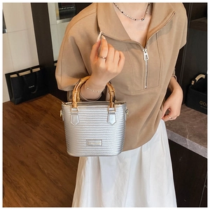 Detail of silver woven bucket bag featuring natural bamboo handles and metal logo tag
