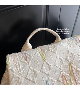Detail showing white embossed monogram handbag with colorful stitching and durable handle