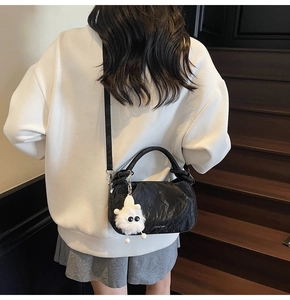 Close-up of black ruched cloud bag with plush pendant on indoor wooden stairs