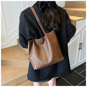 Detail of a brown woven leather tote bag texture on a model wearing a black blazer