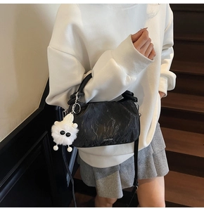Detail of black pleated cloud bag with furry monster charm and logo on a model