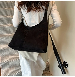 Detailed view of black suede tote bag texture shown on model in a minimalist setting