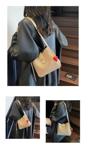 Detail of beige shoulder bag with metal lock and cute red strawberry charm accessory