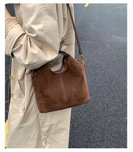 Texture détaillée du sac fourre-tout en daim marron avec coutures et boucles dorées