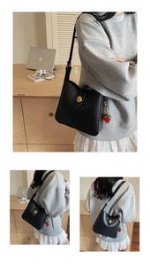 Detail of black shoulder bag featuring golden round clasp and strawberry resin charm