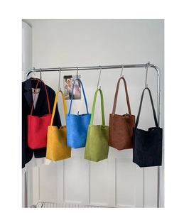 Vertical display of solid color faux suede bucket bags in six vibrant colors hanging on a rack