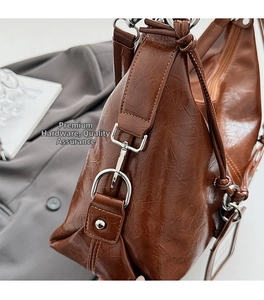 Close-up of brown crinkled leather shoulder bag with polished silver buckles and rivets