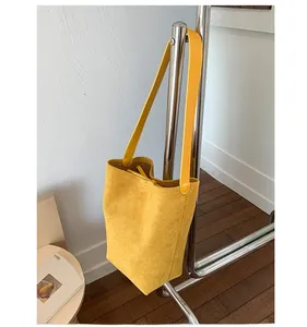Detail view of mustard yellow suede bucket bag with leather strap hanging on a metal rack
