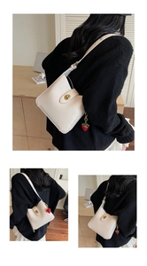 Detail of cream bucket bag with gold twist lock and red strawberry charm accessory