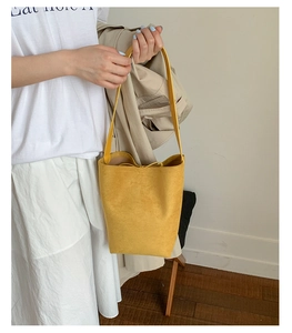 Close-up of bright yellow suede bucket bag with drawstring closure and shoulder strap