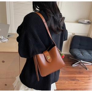 Detail of a brown glossy PU leather bucket bag with retro gold clasp and strawberry charm