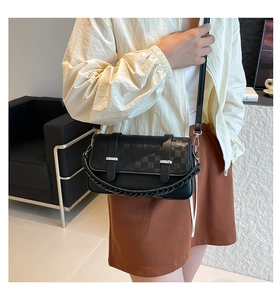 Detail of black crossbody bag featuring textured flap and woven handle in modern setting