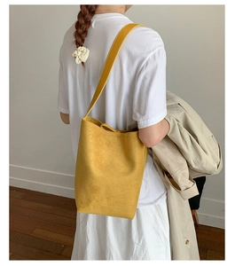 Detail of a minimalist yellow suede bucket bag featuring a wide shoulder strap