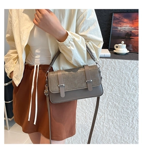 Detail of dark gray bag featuring woven texture flap and metallic decorative buckles