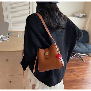 Bolso tipo cubo retro marrón con cierre dorado y colgante de fresa en modelo