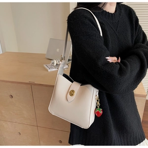 Detalle de bolso bandolera tipo cubo en cuero blanco crema con dije de fresa y cierre dorado
