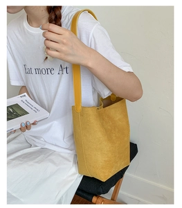 Close-up of a mustard yellow suede bucket bag worn by a model in a casual setting