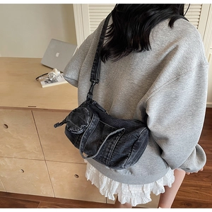 Detail of a black washed denim barrel crossbody bag showing vintage texture and side pocket