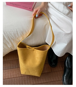 Detail of a bright yellow suede bucket bag featuring a matte finish and minimalist strap