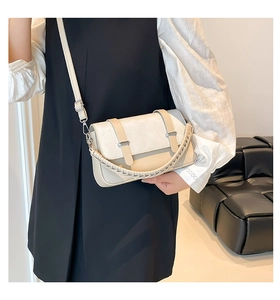 Detail of cream crossbody bag featuring woven top handle and decorative metal buckles