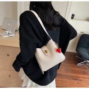 Detalle de bolso saco crema con cierre giratorio dorado y un colgante de fresa elegante