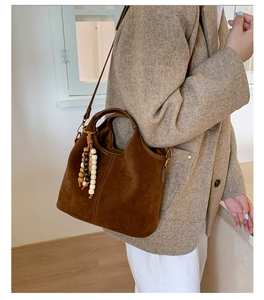 Gros plan sur un sac cabas en daim marron foncé avec pendentif en perles de bois et anses