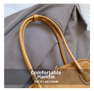 Close-up of brown suede baguette bag featuring reinforced handles and metal zipper detail