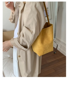 Detail view of a yellow suede bucket shoulder bag worn by model in a minimalist setting