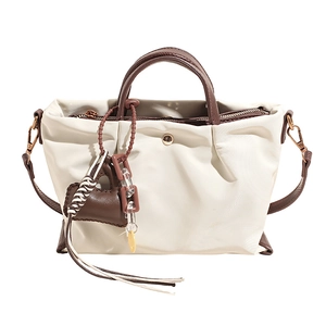 Casual white canvas tote bag with brown leather handles, charm pendant for daily commute.