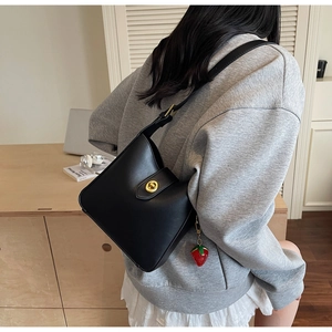 Detalle de bolso cubo de cuero negro con cierre giratorio dorado y un colgante de fresa