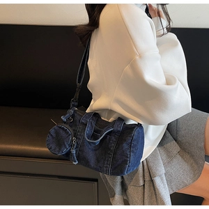 Close-up of a dark blue denim cylinder bag with a matching mini round pouch attachment