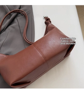 Close-up of dark brown leather handbag featuring knotted strap and silver spherical charms