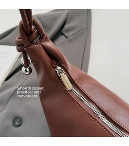 Detail of a brown leather bucket bag featuring a smooth silver zipper and knotted strap