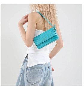 Detail of teal faux crocodile leather shoulder bag with gold logo on white background