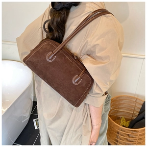 Detail of dark brown suede baguette bag with contrast stitching on female model shoulder