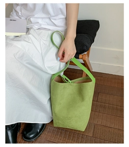 Close-up of a green suede bucket bag styled with a white dress and wooden furniture