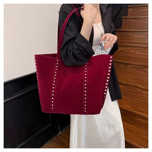 Detail of burgundy suede tote bag with silver studs worn by a model on stairs