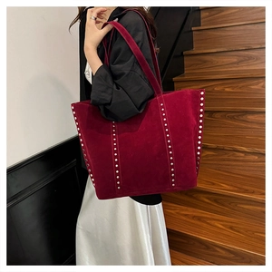 Close-up of burgundy tote bag featuring silver rivet trim and premium suede texture
