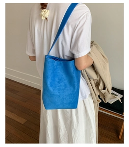Close-up of a blue suede bucket bag worn over the shoulder by a model in a minimal setting
