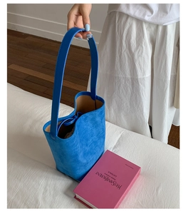 Detail of bright blue suede bucket bag with wide strap and drawstring closure