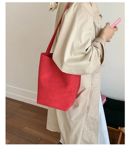 Side view of a large red suede bucket bag paired with a beige trench coat for a stylish look